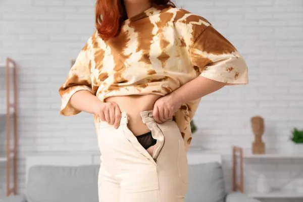 Image of woman trying to do her trousers up after pregnancy weight gain Borehamwood