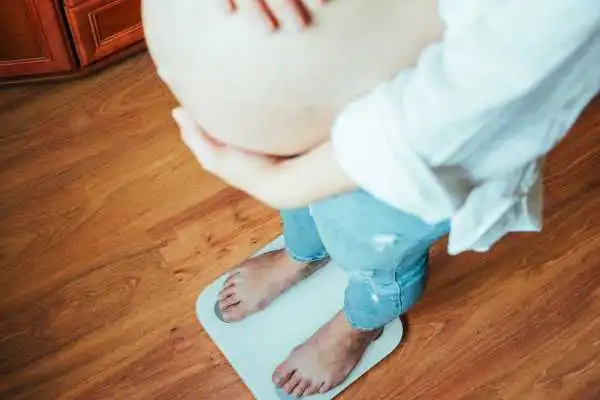 Image of woman weighing herself and experiencing weight gain through pregnancy Borehamwood
